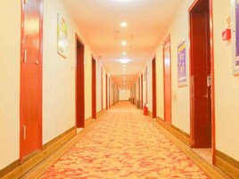 A hotel corridor with doors on both sides, a patterned carpet, and overhead lighting.