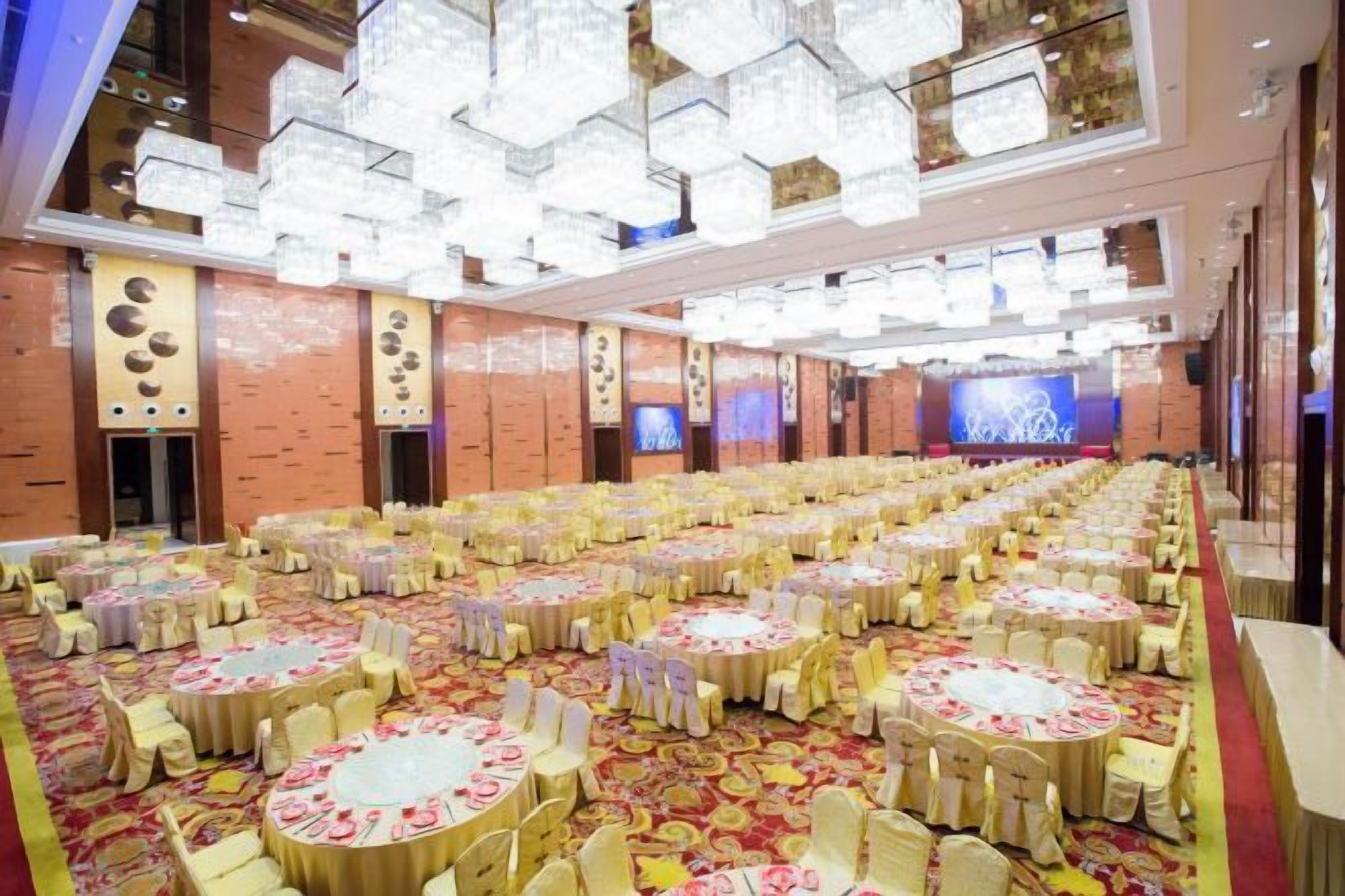A banquet hall with multiple round tables, a stage, and a large screen.