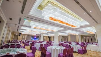 Un salón de banquetes con mesas redondas, sillas moradas y un techo con paneles iluminados.