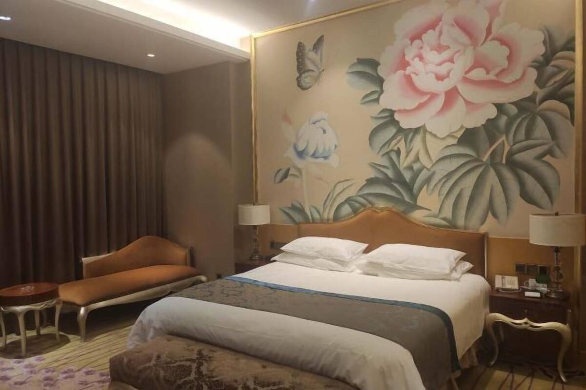 Une chambre d’hôtel avec un lit, une chaise, une table de chevet et un grand décor mural représentant des motifs floraux.