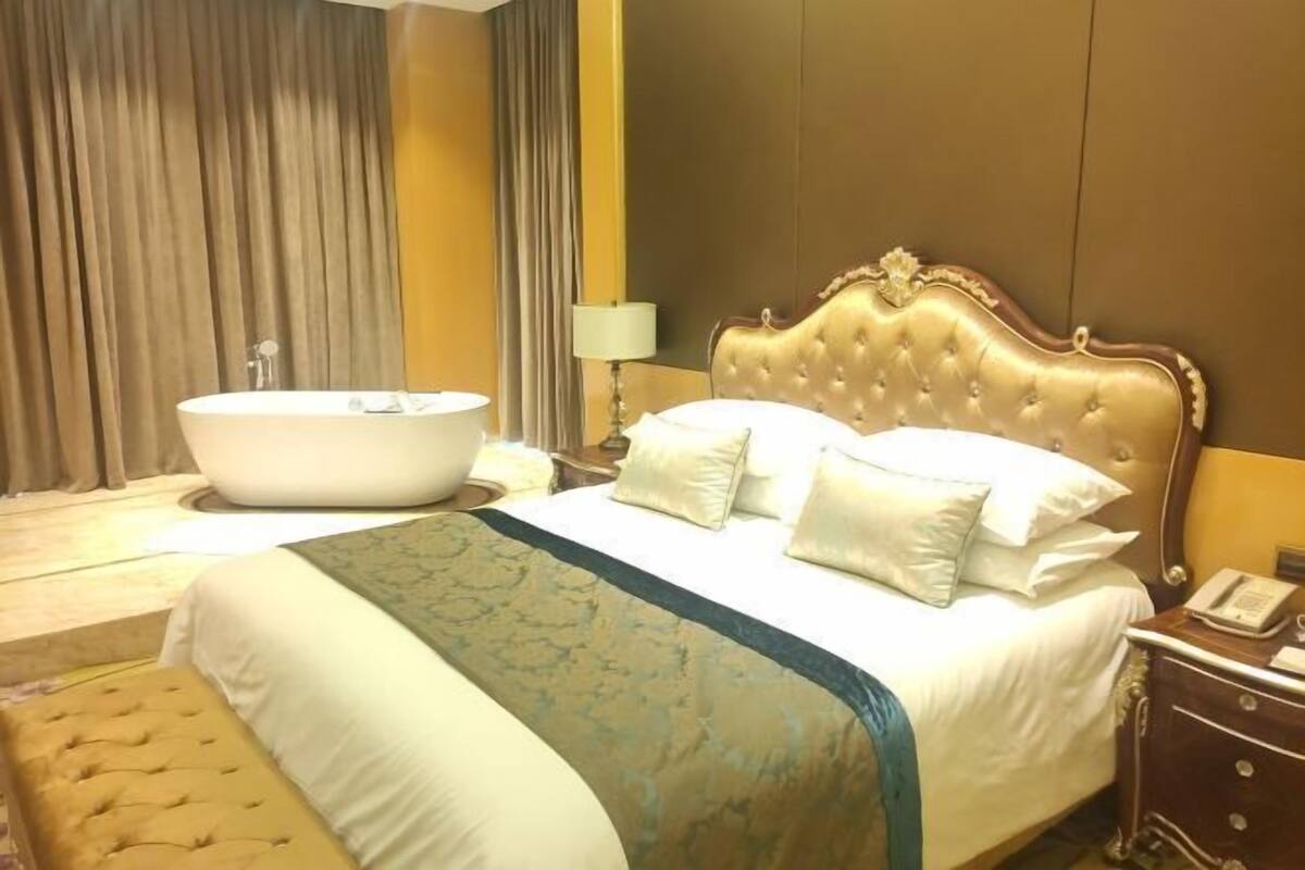 Une chambre d’hôtel avec un grand lit, une baignoire, une table de chevet avec une lampe et un téléphone.