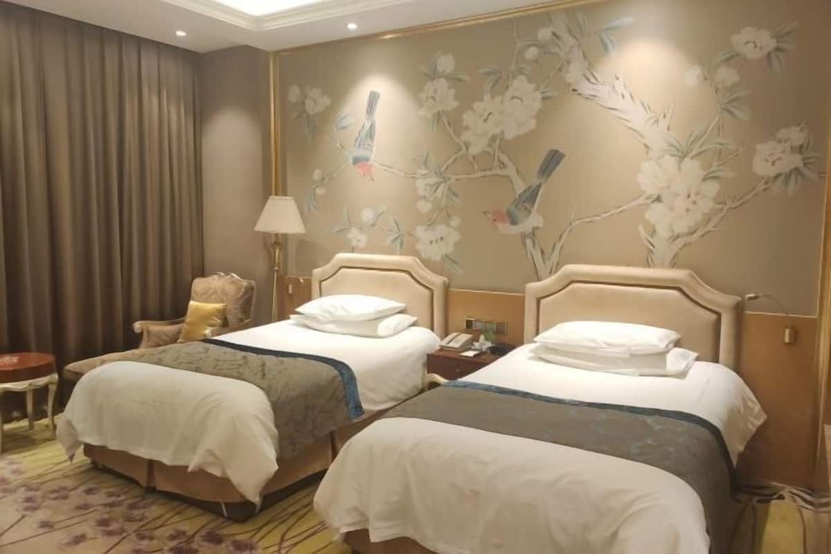 Une chambre d’hôtel avec deux lits, une chaise, une lampe et un mur décoré de motifs floraux et d’oiseaux.