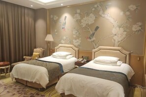 Une chambre d’hôtel avec deux lits, une chaise, une lampe et un mur décoré de motifs floraux et d’oiseaux.