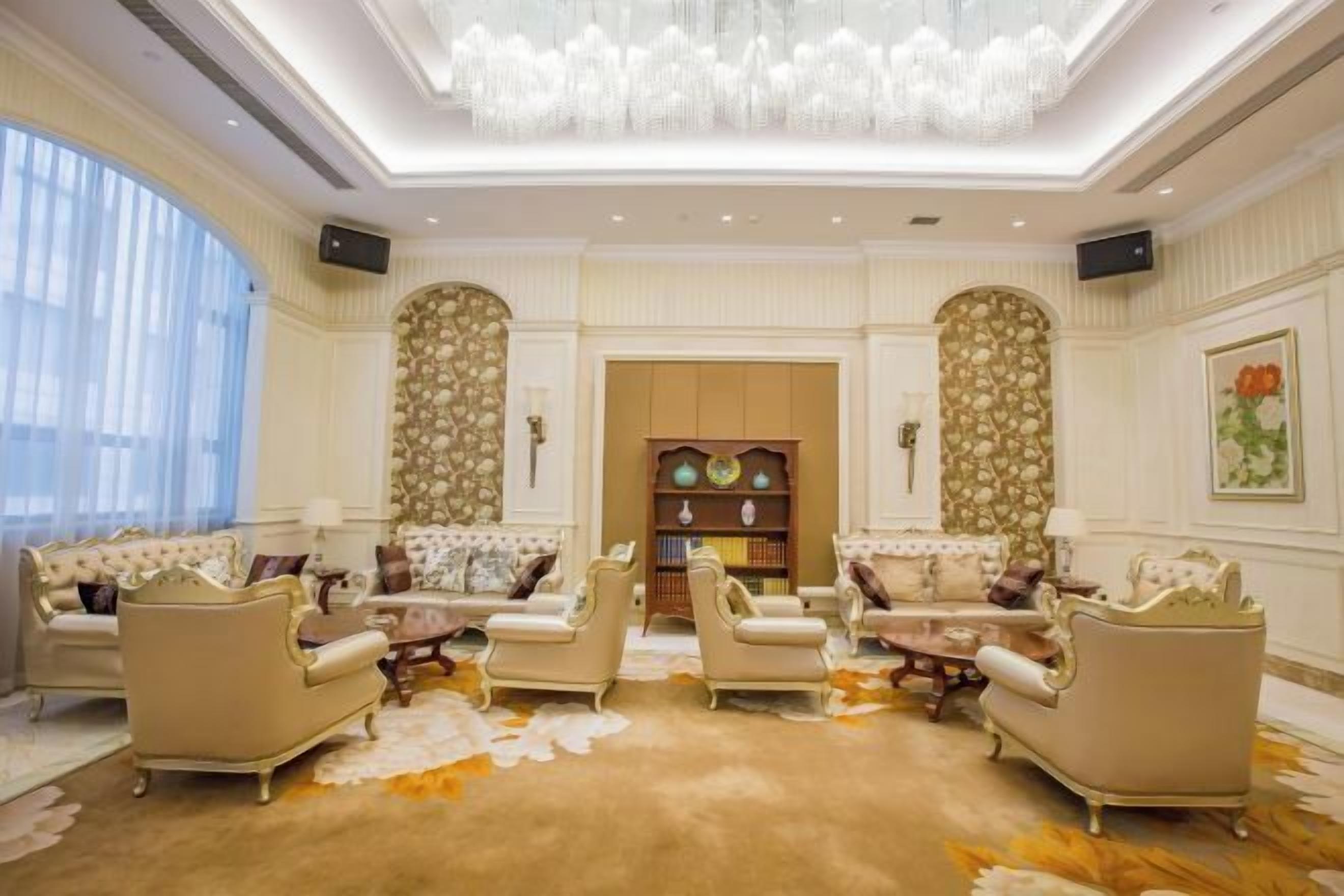 A spacious living room with a high ceiling, ornate wall decorations, and a large chandelier.