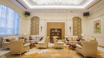A spacious living room with a high ceiling, ornate wall decorations, and a large chandelier.