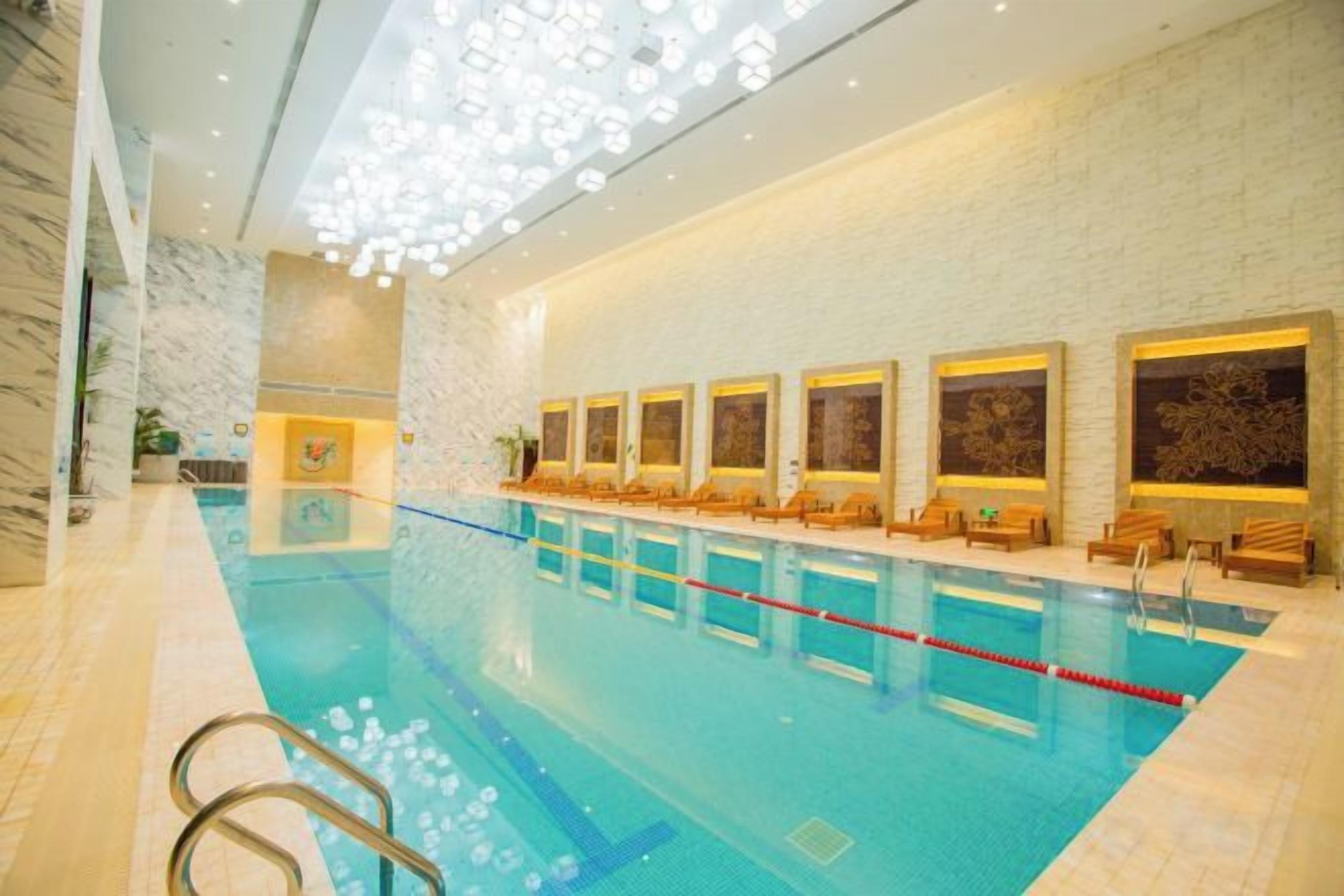 An indoor swimming pool with a marble floor, a long bench along the wall, and a ceiling with a unique light fixture.
