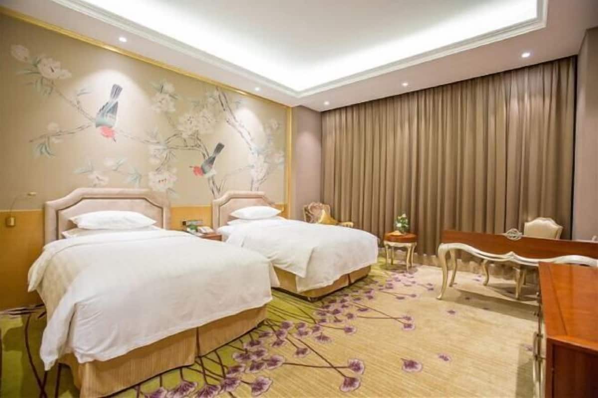 Une chambre d’hôtel avec deux lits, un bureau, une chaise, une petite table et une fresque murale décorative.
