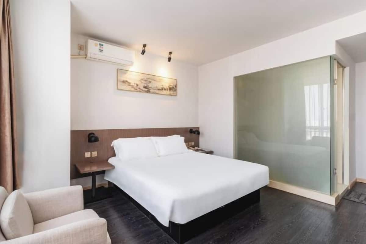 A hotel room with a bed, a nightstand, a chair, a glass door, and a wall-mounted air conditioner.