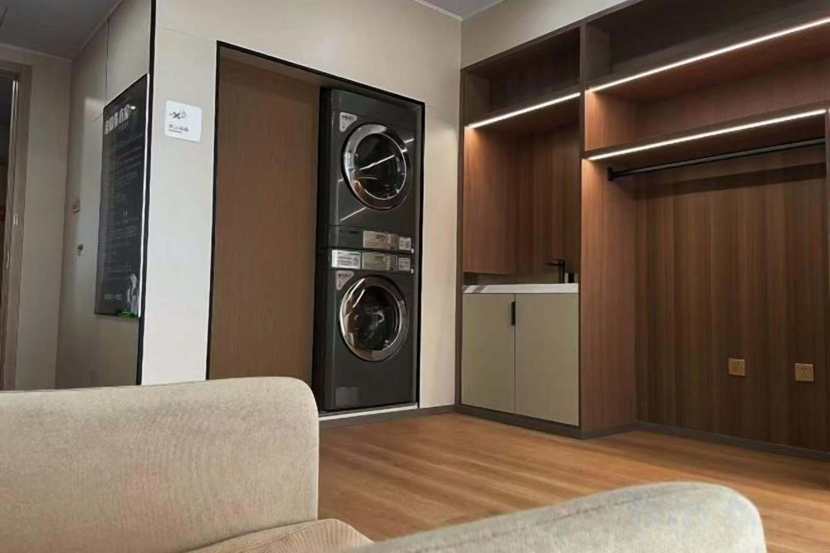 A compact hotel room with a built-in washer and dryer, a kitchenette, and a wooden floor.