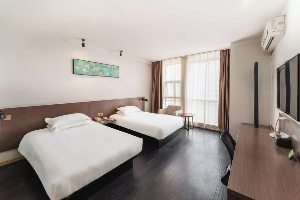 A hotel room with two beds, a desk, a chair, a TV, and a painting on the wall.