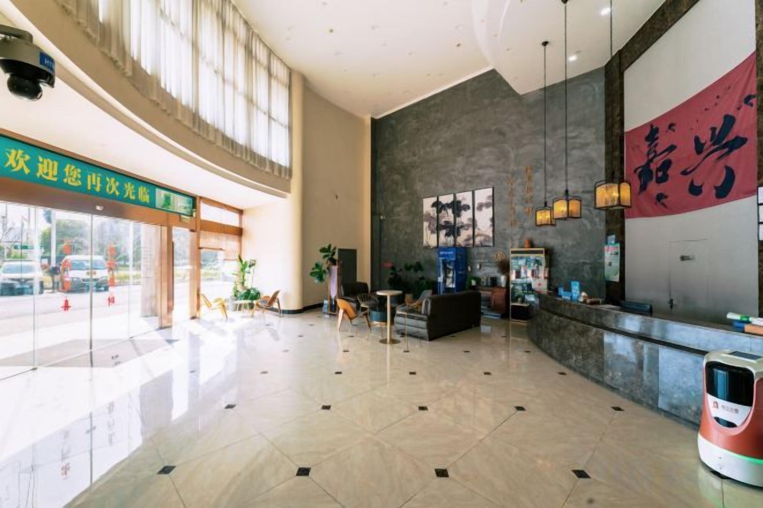 A hotel lobby with a reception desk, seating area, and a large window allowing natural light.
