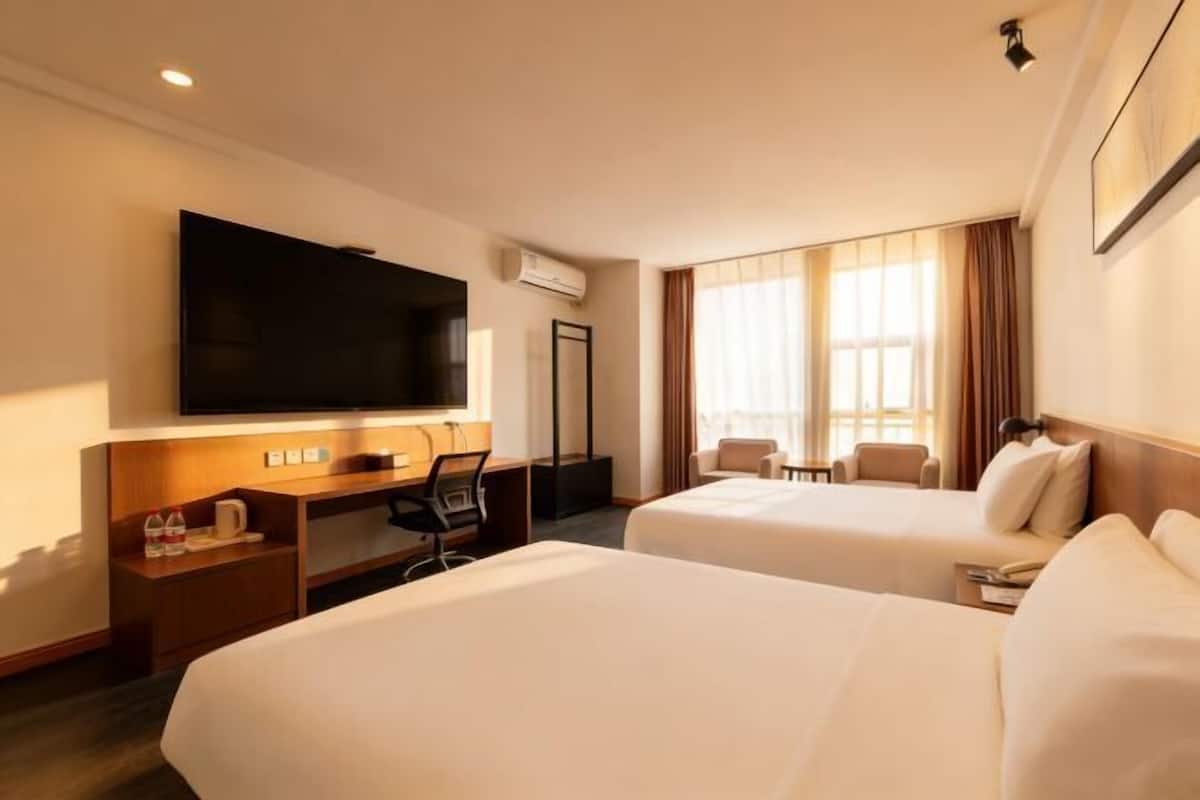 A hotel room with two beds, a desk, a chair, a TV, and a window with curtains.