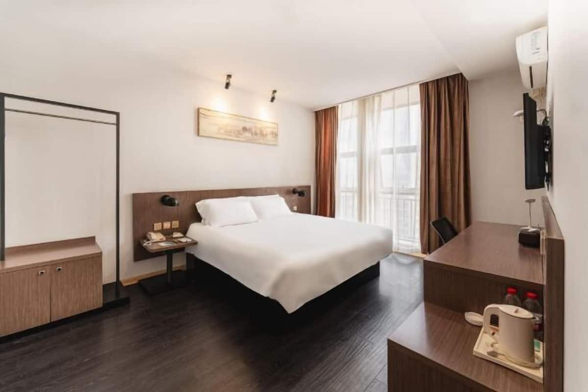 A hotel room with a bed, bedside table, desk, chair, and a window with curtains.