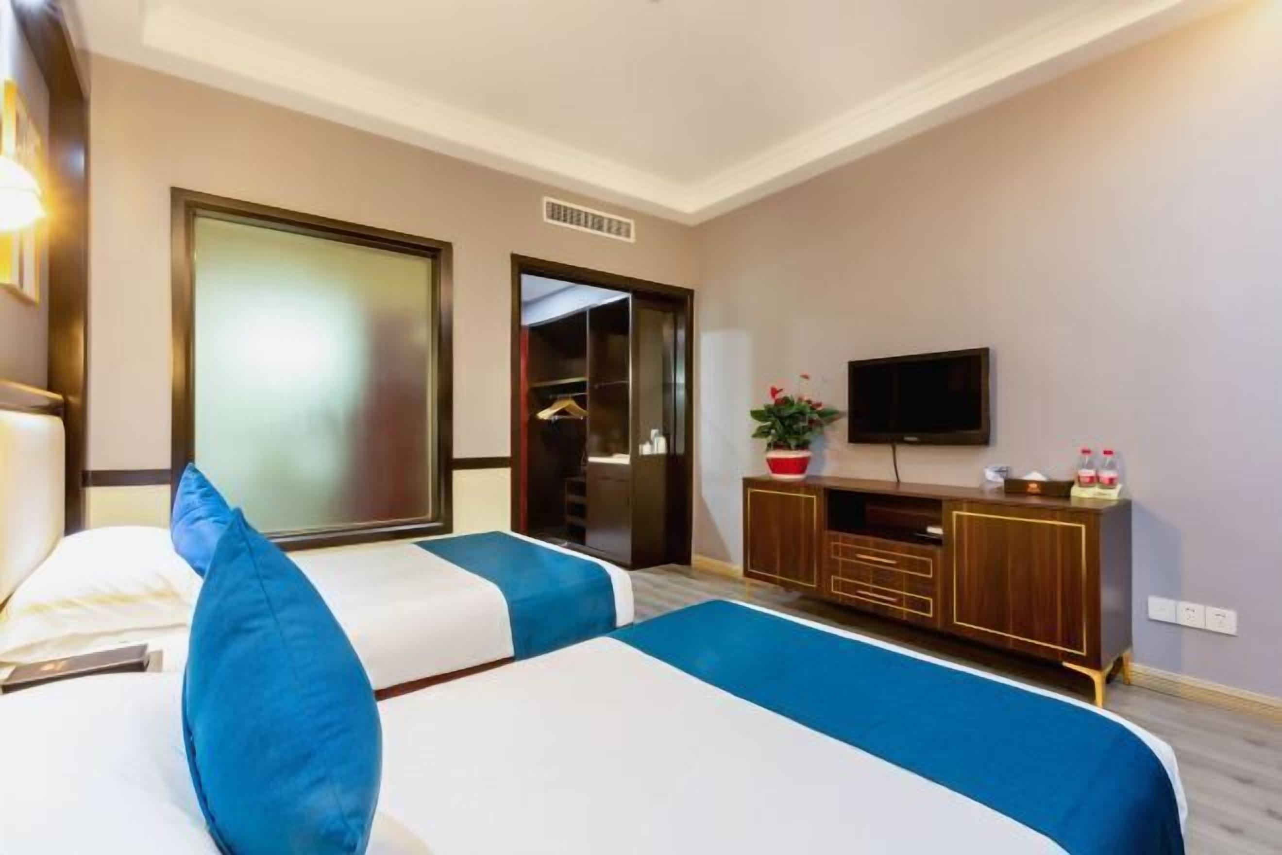 A hotel room with two beds, a TV, a wardrobe, and a plant.
