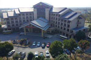 A multi-story hotel with a central entrance, parking lot, and surrounding trees. - Guanfeng Holiday Hotel (Tongxiang)