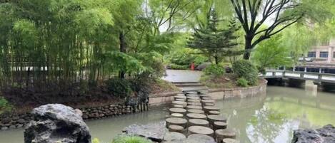 Un jardin paisible avec un pont de pierre enjambant un étang, le tout entouré d’une végétation luxuriante et d’arbres.