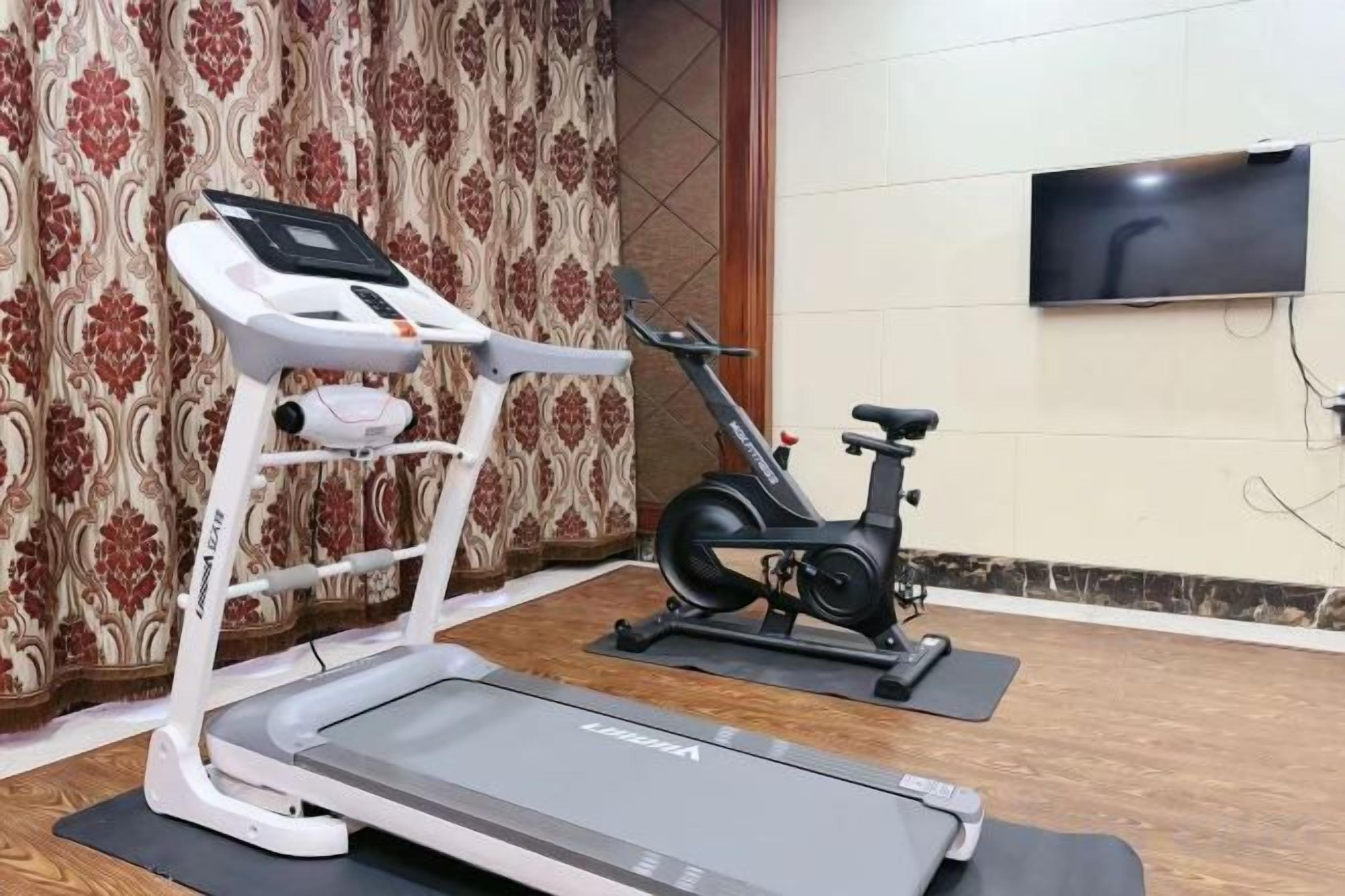 Een huisgymnasium met een loopband, elliptische trainer en een hometrainer.