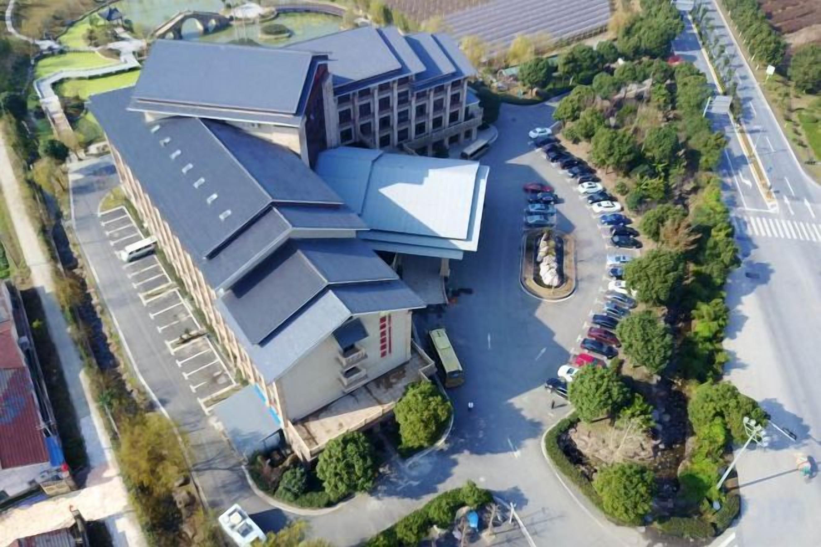 Vue aérienne d’un bâtiment avec un parking et des espaces verts environnants.