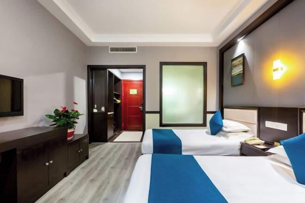 Une chambre d’hôtel avec deux lits, un bureau, une télévision et une porte rouge donnant sur une salle de bain.