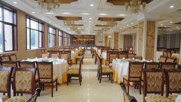 A spacious dining hall with rows of tables and chairs, large windows, and chandeliers.