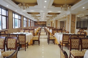 A spacious dining hall with rows of tables and chairs, large windows, and chandeliers. - Guanfeng Holiday Hotel (Tongxiang)