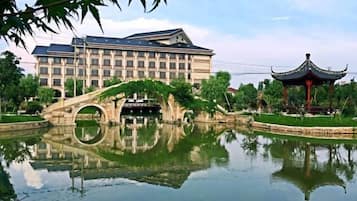 Um edifício refletido em um lago, uma ponte e um pavilhão tradicional.