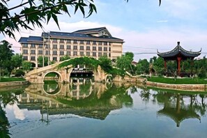 Un edificio con su reflejo en un estanque, un puente y un pabellón tradicional.