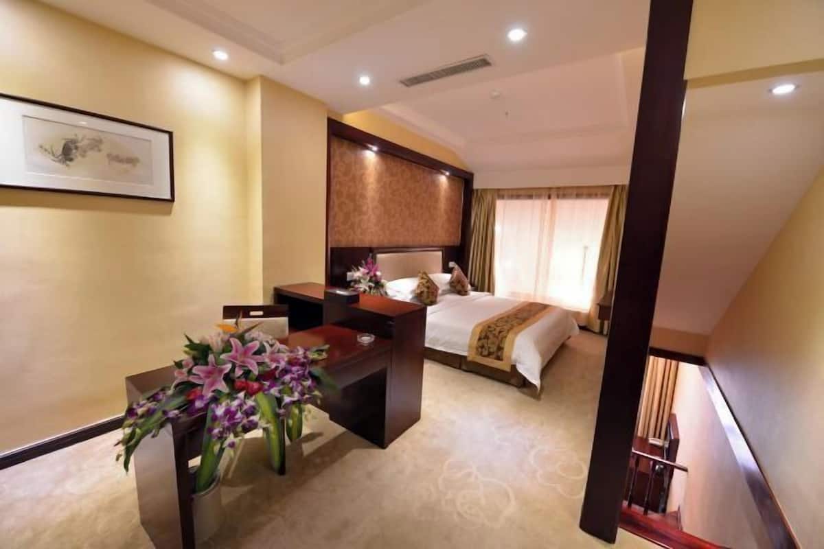 Une chambre d’hôtel avec un lit, un bureau et une chaise. Un vase rempli de fleurs est posé sur le bureau.