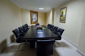 Un salón de conferencias con una larga mesa, sillas negras y dos cuadros en las paredes.