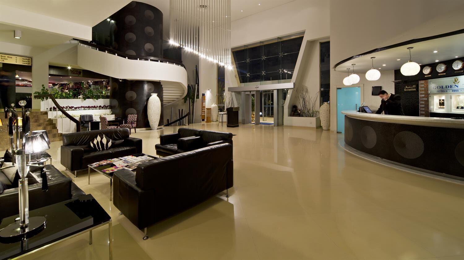 A modern hotel lobby with a reception desk, seating area with sofas, and a staircase leading to upper floors.