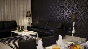 En moderne stue med en sort lædersofa, et hvidt sofabord og et spiseområde med et glasbord dækket til to personer.