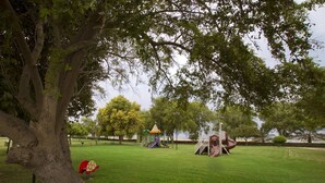 En park med legeplads, et stort træ og græsplæne.