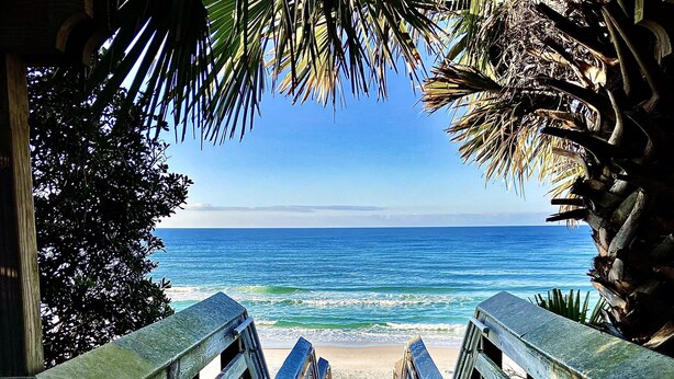 A wooden staircase leading to a beach with a clear view of the ocean.