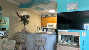 A kitchen with a bar area, a microwave, and a TV. There are wicker chairs and a plant.