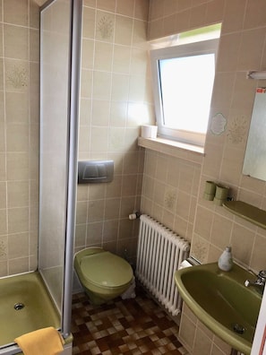 A bathroom with a toilet, sink, shower, and a window.