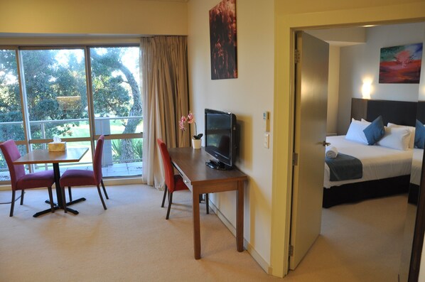 A hotel room with a bed, a TV, a dining table with chairs, and a view of the outdoors. - Ocean Breeze Hotel (Auckland)