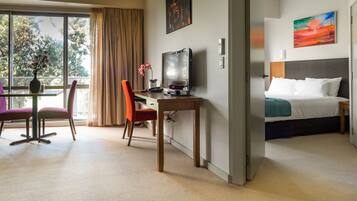 Habitación de hotel con una cama, un escritorio con ordenador, una silla, una ventana con cortinas y un cuadro en la pared.