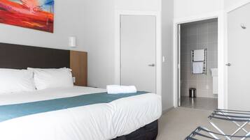 A hotel room with a bed, a wall-mounted painting, a door leading to a bathroom, and a laundry basket.