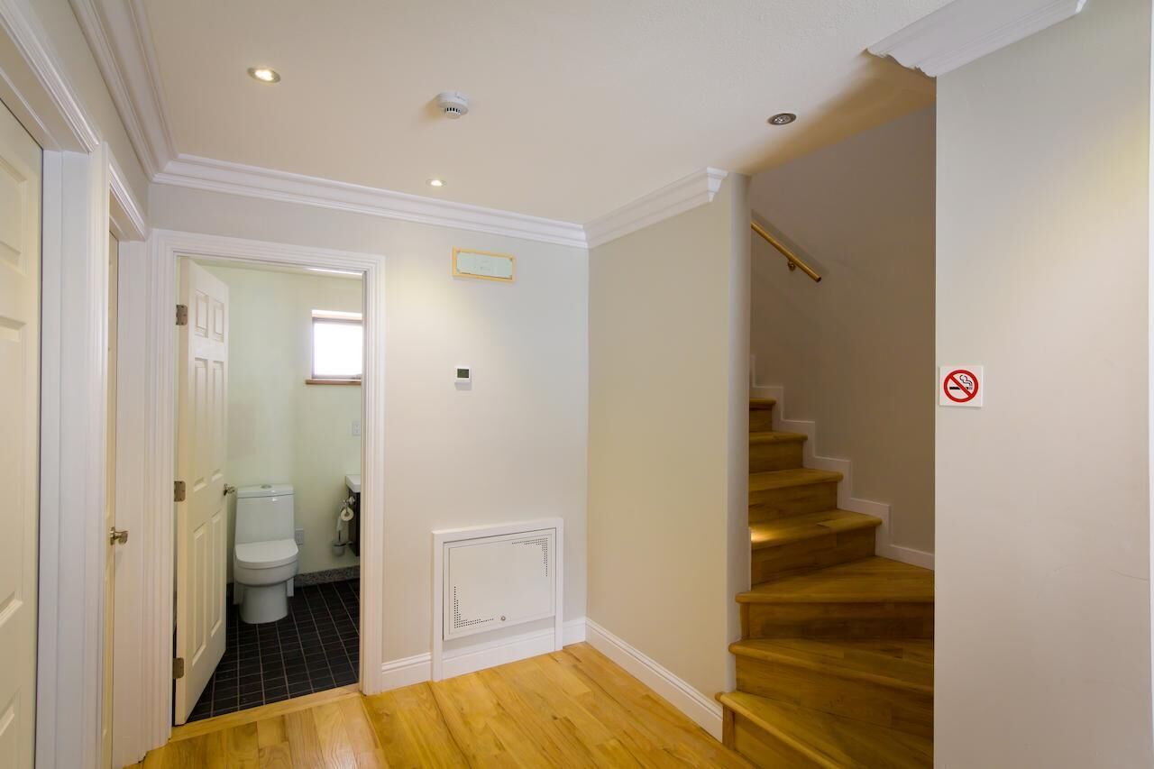 A hallway with a wooden staircase, a white door, and a view into a bathroom.