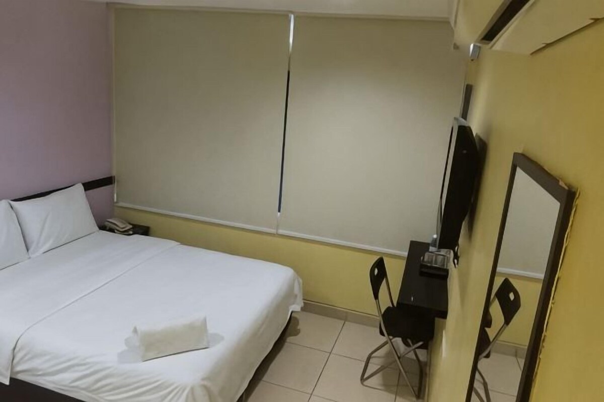 A hotel room with a bed, a desk, a chair, a mirror, and a window.