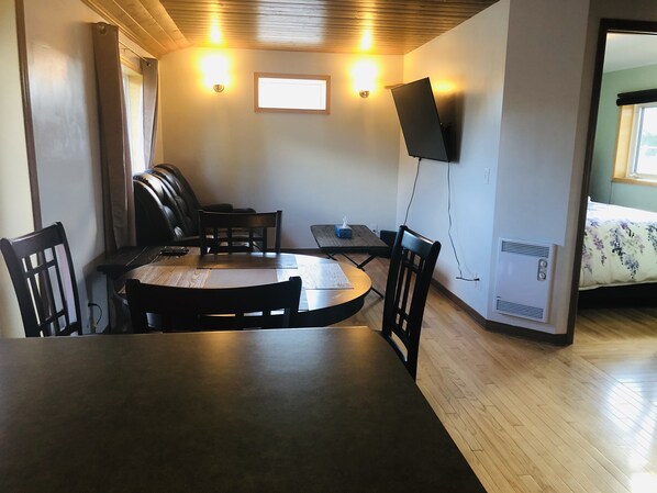 Un coin repas comprenant une table ronde, des chaises, un téléviseur à écran plat fixé au mur et une fenêtre avec des rideaux.