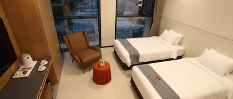 A hotel room with two beds, a desk with a coffee maker, a chair, and a small table with a plant.