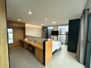 Ein modernes Hotelzimmer mit eigenem Bad, einem Bett, einem Schreibtisch und einem großen Fenster mit Blick auf die Stadt.