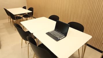 Una sala de conferencias moderna con mesas blancas y sillas negras, equipada con computadoras portátiles.
