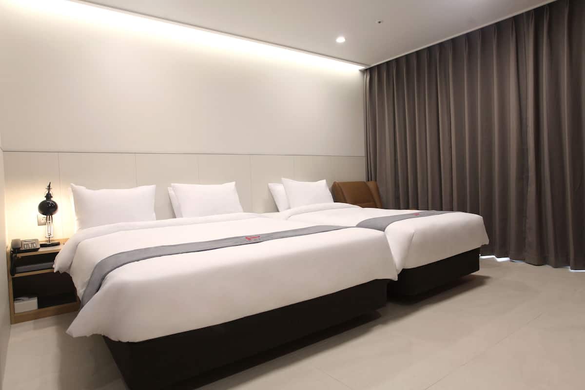 Een moderne hotelkamer met een groot bed, een nachtkastje met een lamp, en uitzicht op de stad door het raam.