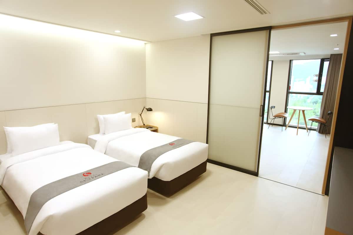 Hotelkamer met twee bedden, een nachtkastje, een lamp en een schuifdeur naar een balkon met stoelen.