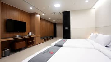 A modern hotel room with two beds, a flat-screen TV, a wooden desk, and a small seating area.