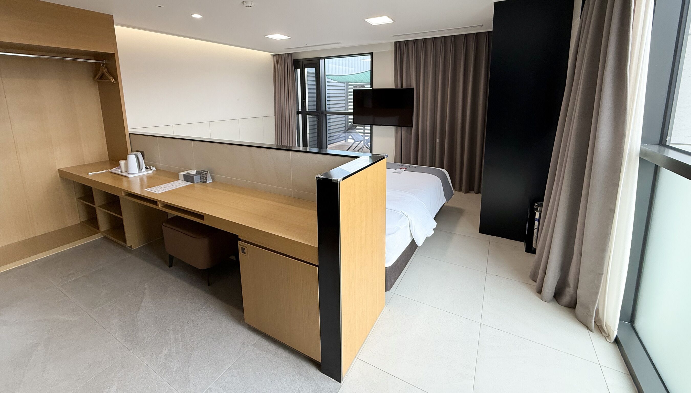 Una habitación de hotel compacta con un escritorio de madera, una cama, un televisor y un ventanal grande.