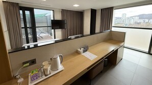 Een hotelkamer met een lang houten bureau, een flatscreen televisie aan de muur, een raam met gordijnen en uitzicht op de stad.