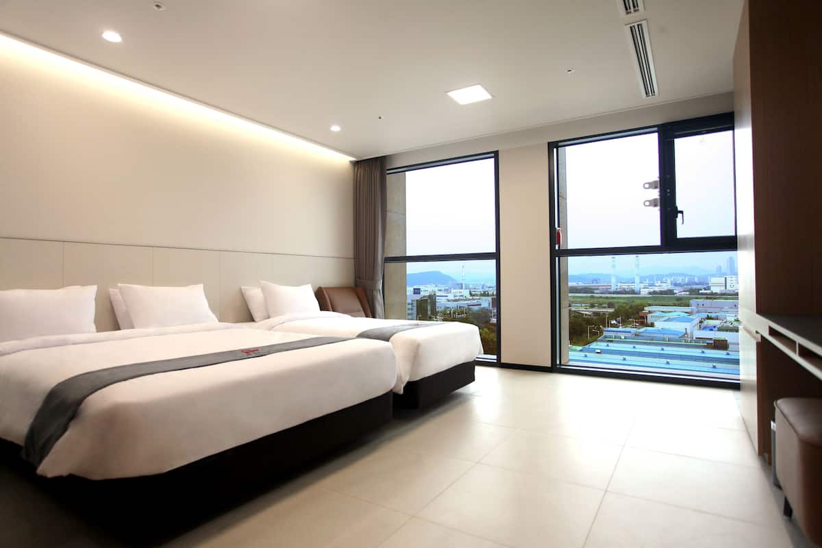 Een moderne hotelkamer met een groot bed, uitzicht op de stad en een raam met zonwering.